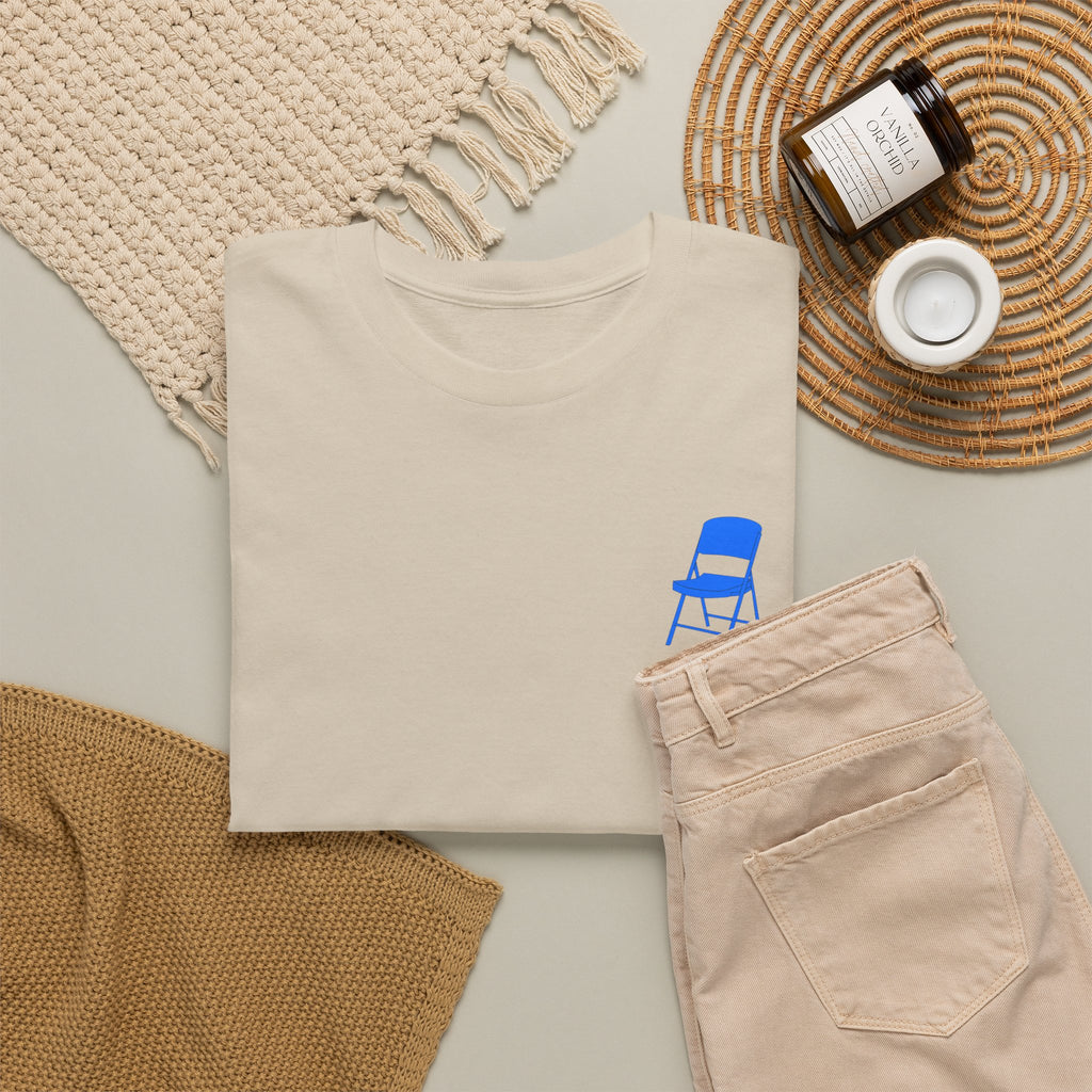 Beige sweatshirt with blue chair graphic, beige pants, and decorative items on a light surface.