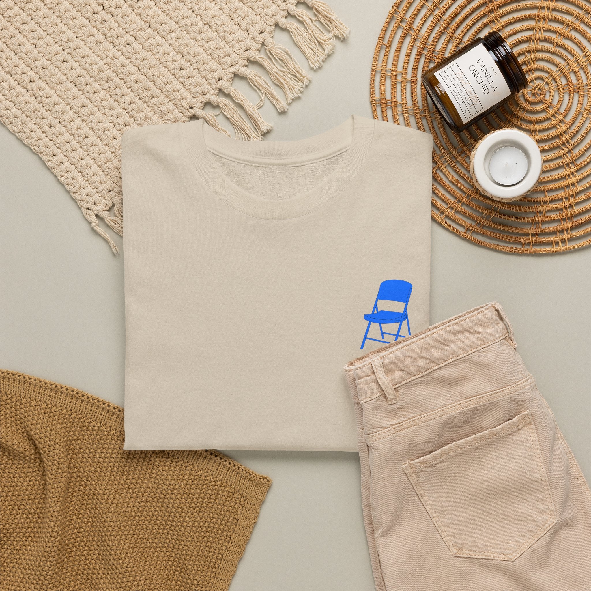 Beige sweatshirt with blue chair graphic, beige pants, and decorative items on a light surface.